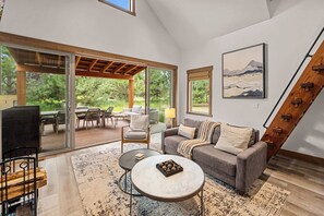 A spacious living area with a large sliding glass door leading to an outdoor patio, a comfortable sofa, a coffee table, and a television. - Wilderness Club Park Cottage (Eureka)