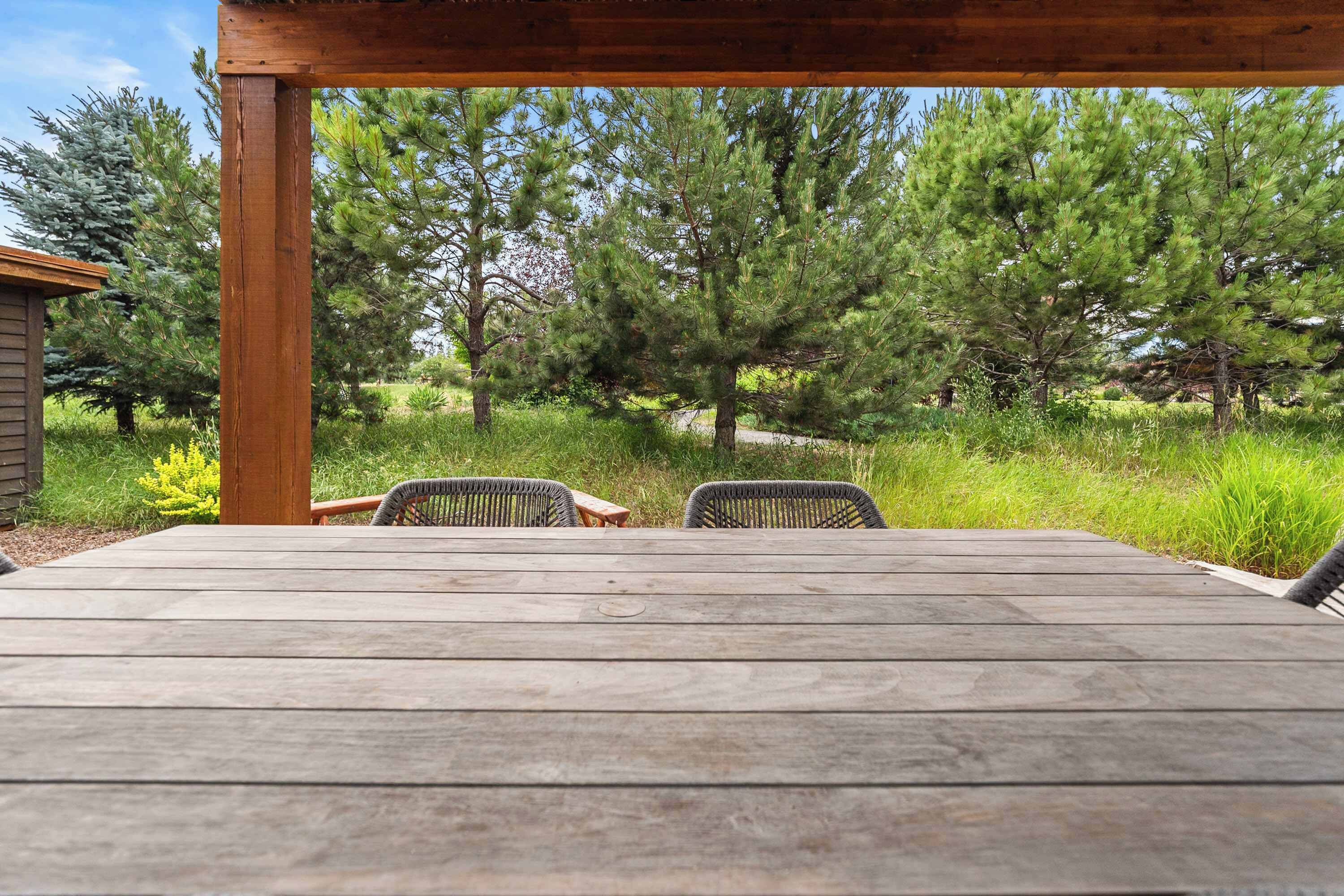 An outdoor wooden deck with two wicker chairs and a table, surrounded by a grassy area and trees.