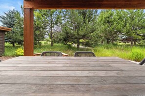 An outdoor wooden deck with two wicker chairs and a table, surrounded by a grassy area and trees. - Wilderness Club Park Cottage (Eureka)