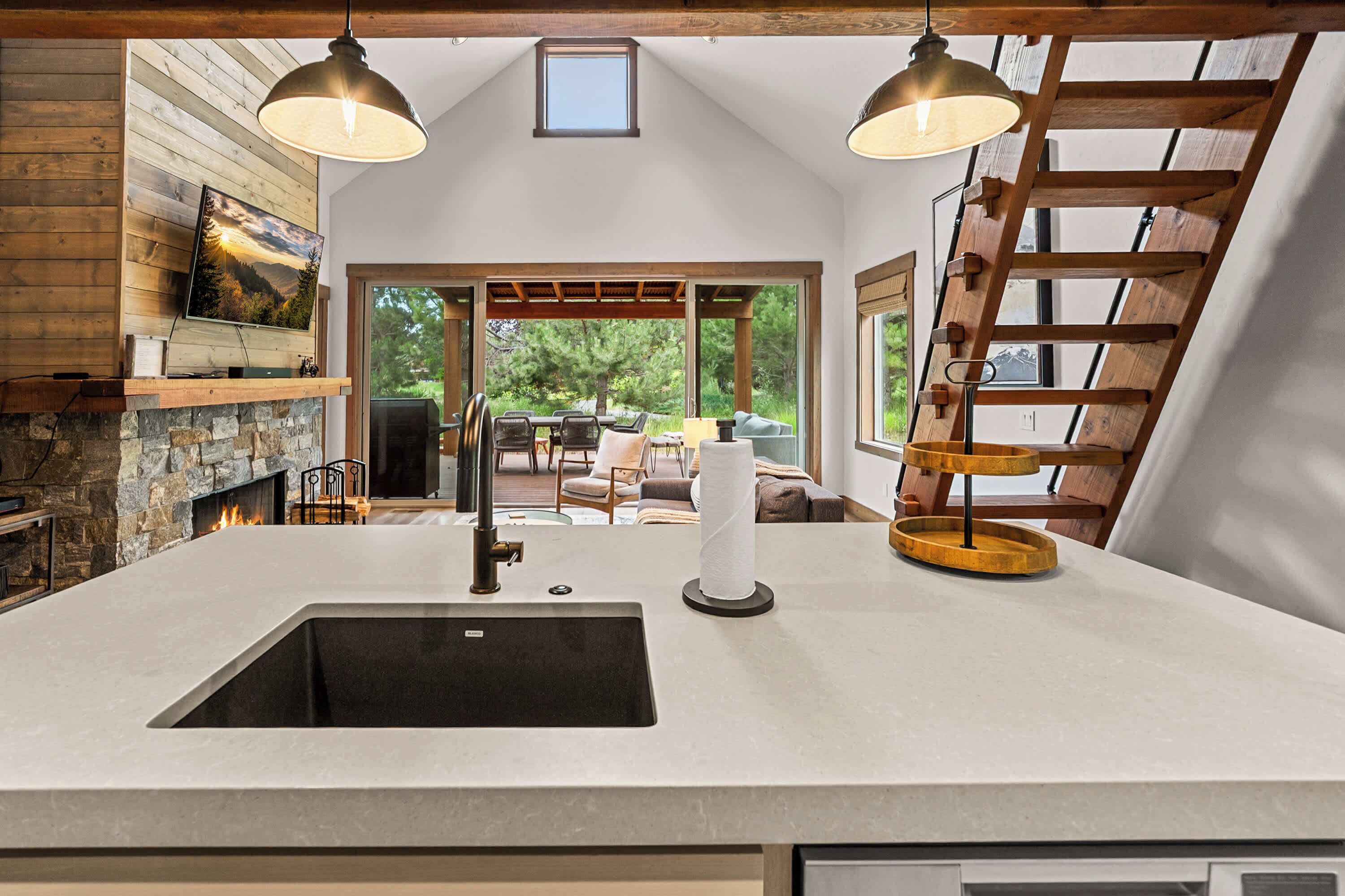 A kitchen with a stone fireplace, a large island with a sink, and a view of the outdoors.