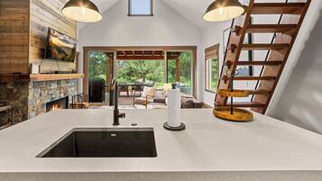 A kitchen with a stone fireplace, a large island with a sink, and a view of the outdoors.
