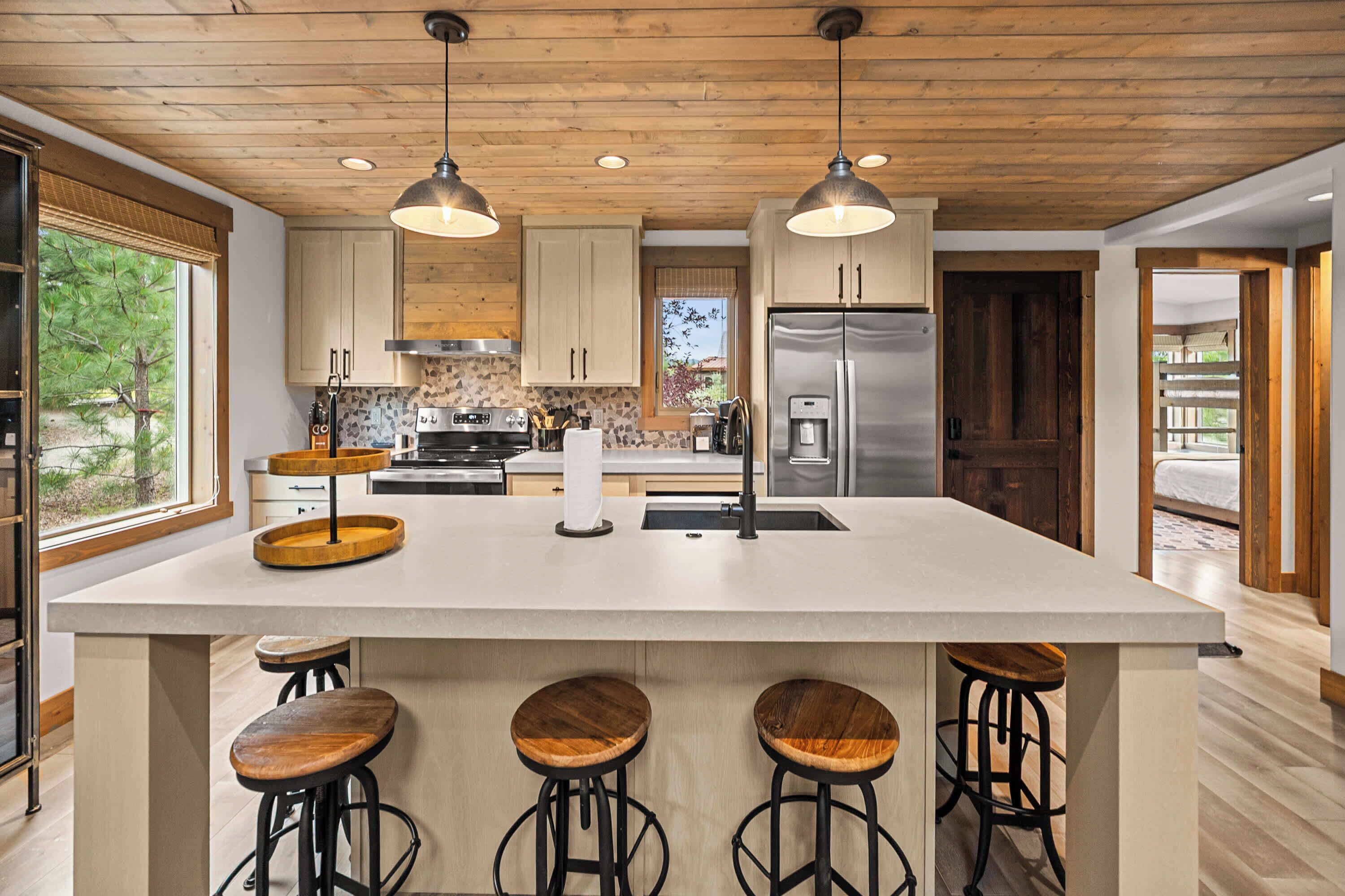 A modern kitchen with a large island, bar stools, wooden cabinets, and a stainless steel refrigerator.