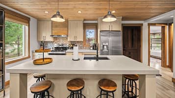 A modern kitchen with a large island, bar stools, wooden cabinets, and a stainless steel refrigerator.
