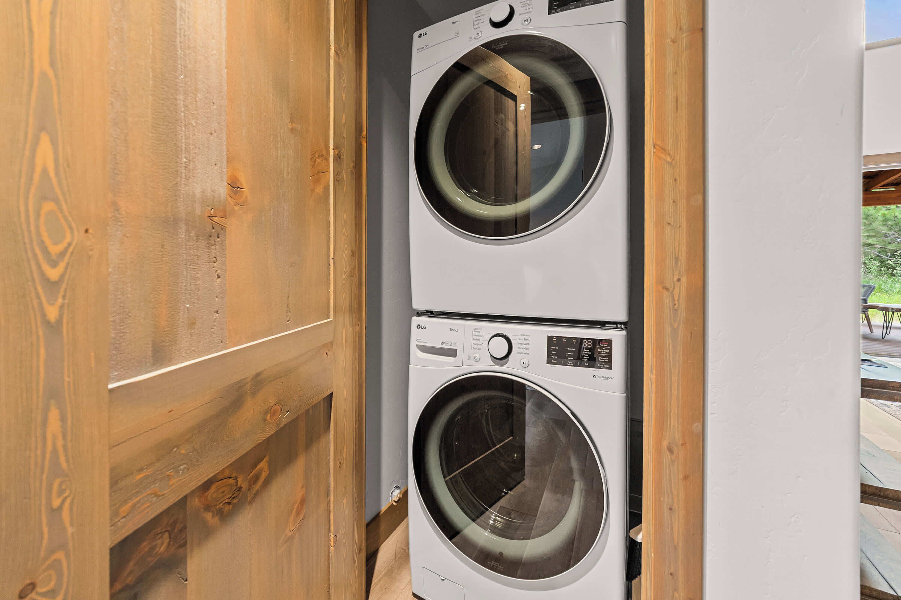 A stacked washer and dryer unit with a wooden door and a view of an outdoor area.