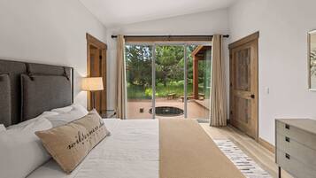 A bedroom with a bed, a nightstand, a lamp, a wooden bench, and a view of an outdoor deck.