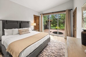 A bedroom with a bed, a nightstand, a lamp, and a view of a garden through a sliding glass door. - Wilderness Club Park Cottage (Eureka)