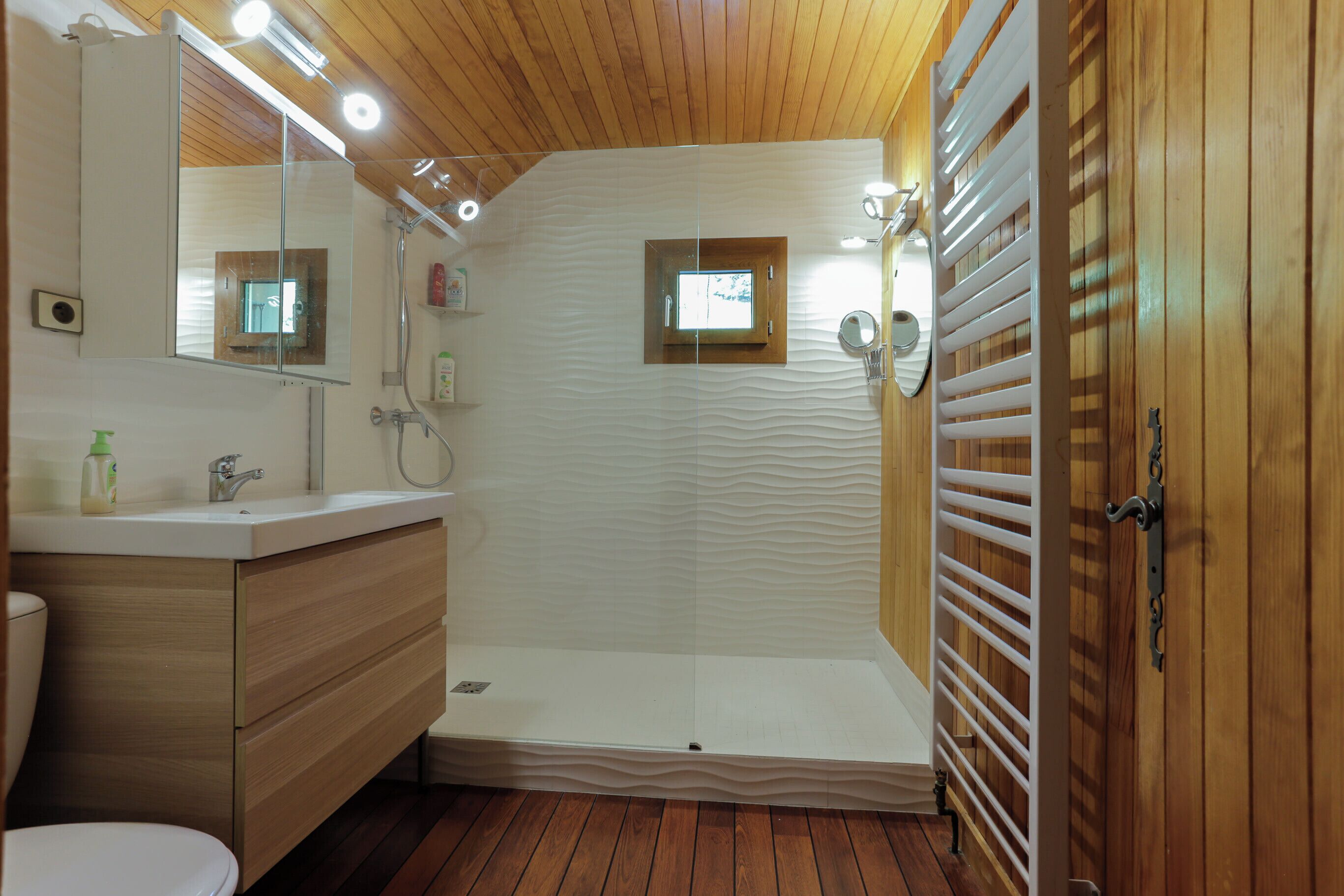 Une salle de bain moderne avec un plafond en bois, une douche à l’italienne, un meuble-lavabo avec un miroir et des toilettes.