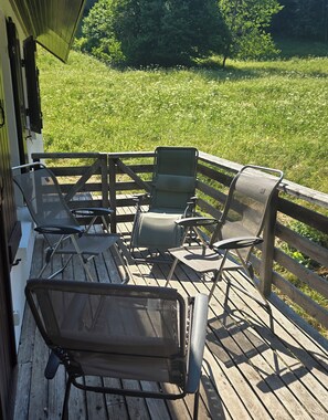Eine Holzterrasse mit Gartenmöbeln, darunter Stühle und ein Tisch, mit Blick auf eine Wiese.