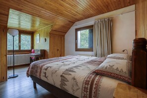 Ein Schlafzimmer mit Holzboden, einem großen Bett mit gemusterten Betttextilien, einem Schreibtisch mit Lampe und einem Fenster mit Vorhängen.