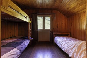 Eine Holzhütte mit zwei Etagenbetten, Holzbalkendecke, einem Fenster mit Blick ins Grüne und einer Heizung.
