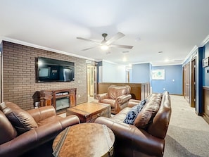 A living room with leather sofas, a coffee table, a fireplace, and a television mounted on the wall. - Luxury 8BR ChampionsGate Villa w/ Pool & Theater (Davenport)