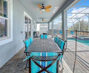 A covered patio with a dining table and chairs, a ceiling fan, and a view of a swimming pool. - Luxury 8BR ChampionsGate Villa w/ Pool & Theater (Davenport)