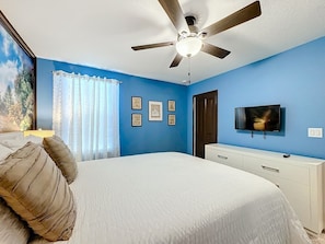 A bedroom with a bed, a ceiling fan, a television, and framed pictures on the wall. - Luxury 8BR ChampionsGate Villa w/ Pool & Theater (Davenport)