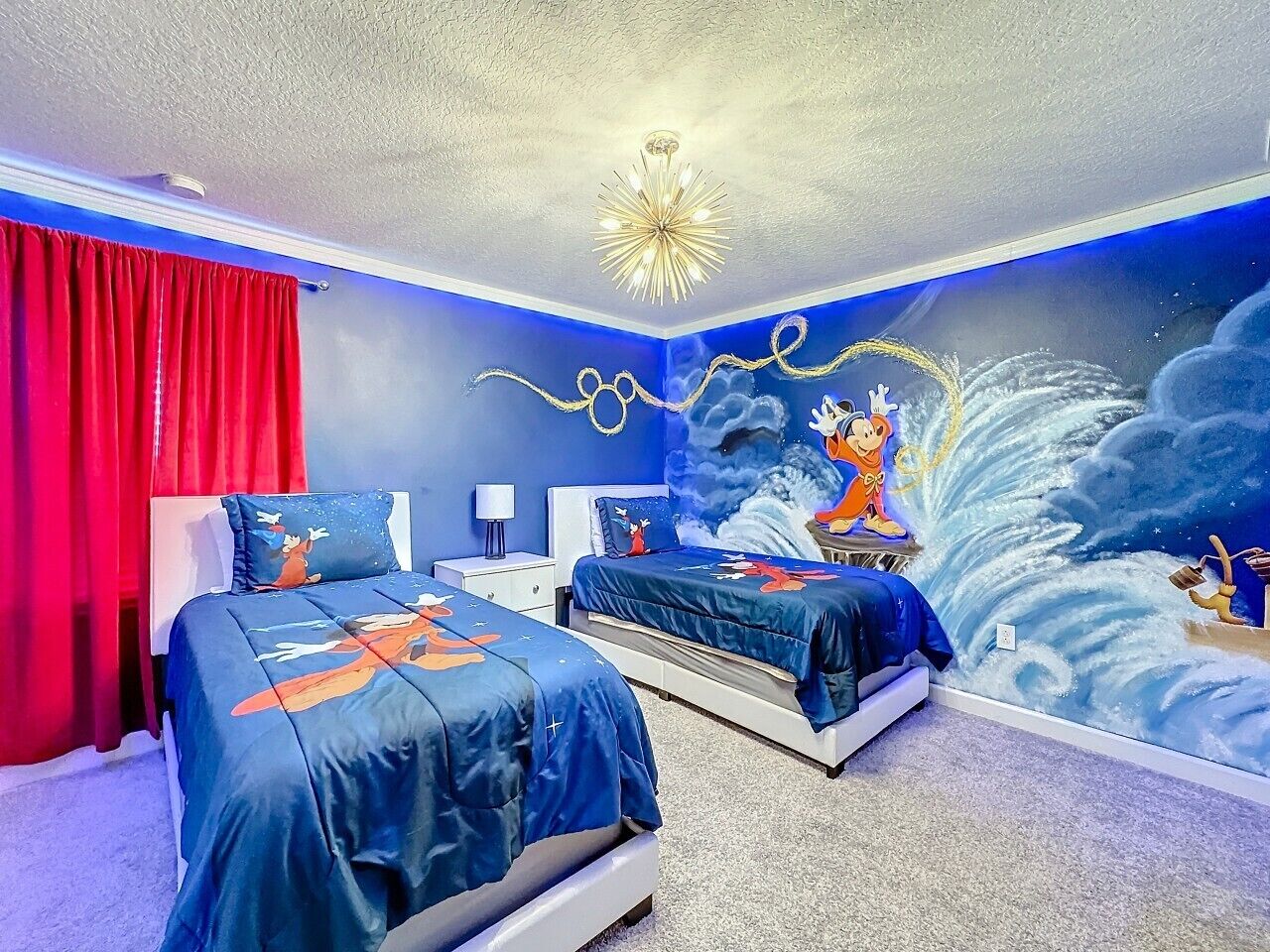 Un dormitorio con dos camas, una cortina roja, una lámpara de araña y un mural en la pared.