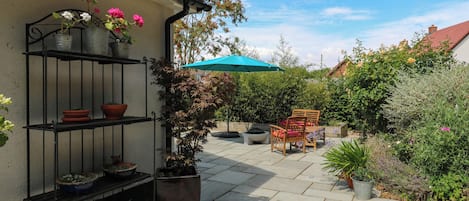 A patio with a stone floor, a wooden table with chairs, and a blue umbrella.
