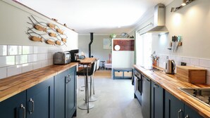 A modern kitchen with dark cabinets, a wooden countertop, and a fish wall art piece. - The Annexe @ Shotley Cottage (Ipswich)