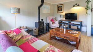 A cozy living room with a sofa, a coffee table, a television, and a fireplace. - The Annexe @ Shotley Cottage (Ipswich)