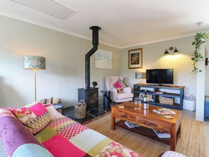 A cozy living room with a sofa, a coffee table, a television, and a fireplace. - The Annexe @ Shotley Cottage (Ipswich)
