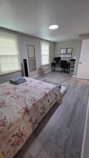 A bedroom with a bed, a desk, a chair, and a door.