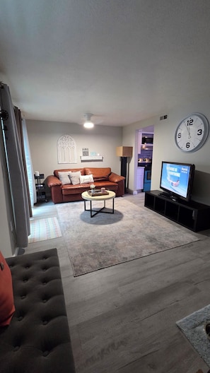 A living room with a brown leather sofa, a coffee table, a television, and a clock on the wall.