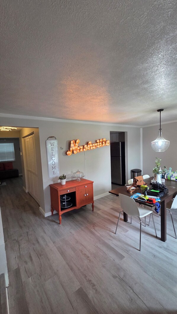 A modern kitchen with a built-in refrigerator, a wooden dining table, and a neon sign that reads 'Welcome to Nashville.'
