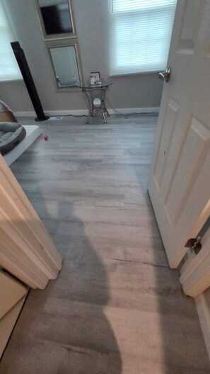 A hallway with a wooden floor, a small table with a vase, and a door on the right.