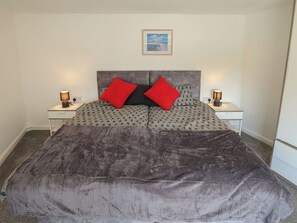 Una cama con cabecera estampada, dos mesitas de noche con lámparas y un cuadro en la pared.