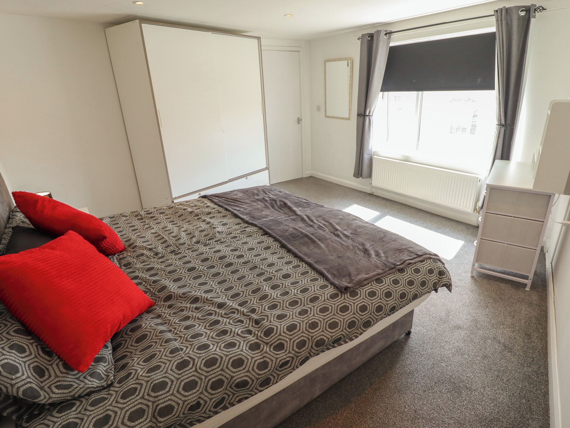 Un dormitorio con cama, armario, radiador y ventana con cortinas.