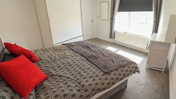 Un dormitorio con cama, armario, radiador y ventana con cortinas.