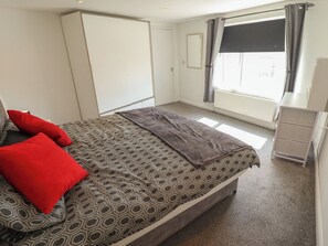 Un dormitorio con cama, armario, radiador y ventana con cortinas.