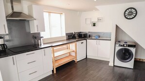 Una cocina moderna con gabinetes blancos, horno integrado, cafetera y lavadora.