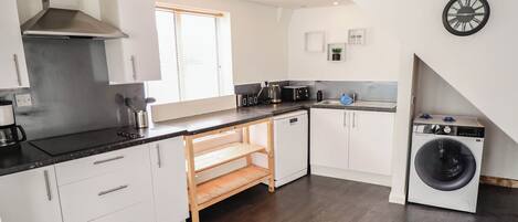 A modern kitchen with white cabinets, a built-in oven, a coffee maker, and a washing machine.