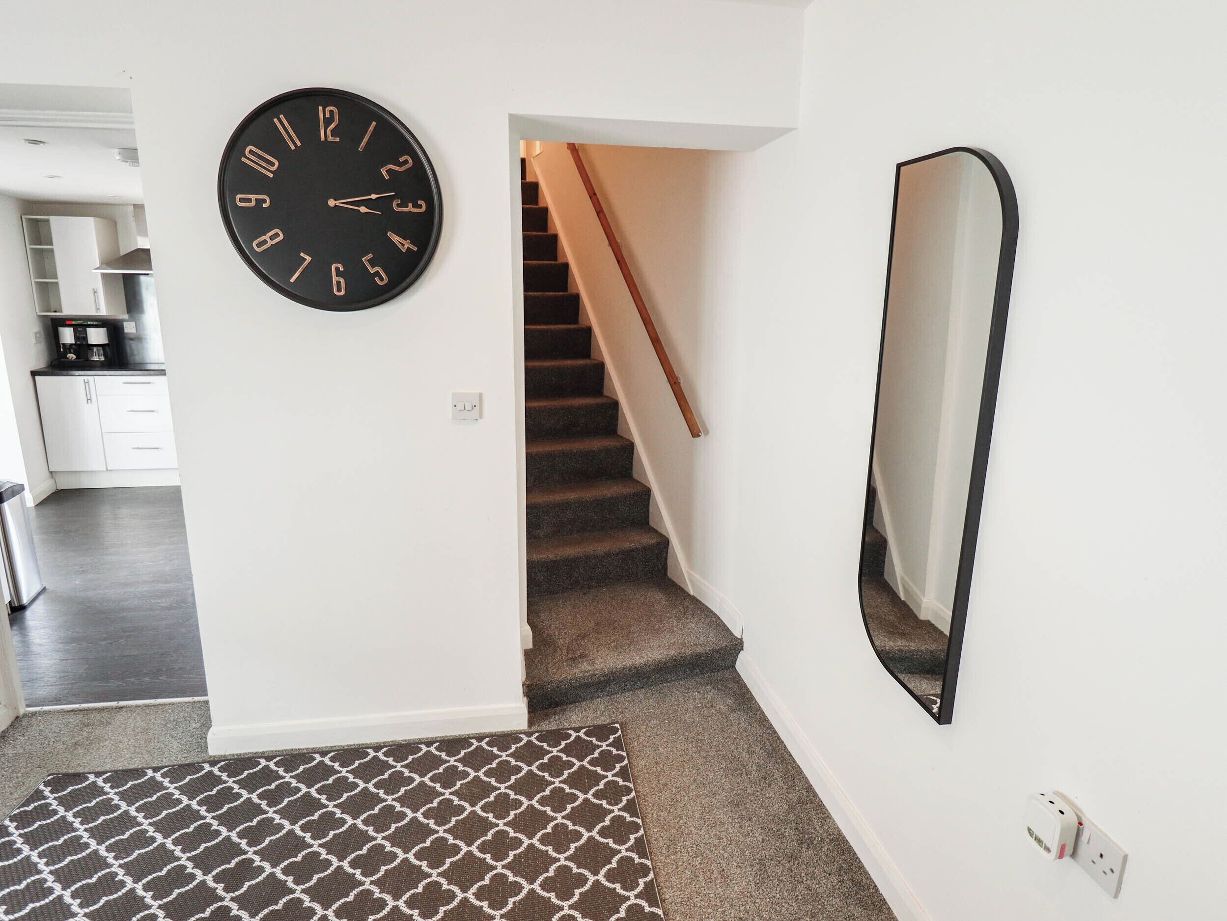 Una escalera con barandilla, un reloj de pared negro y un espejo.