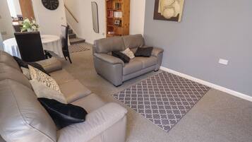 A living room with a grey sofa, a patterned rug, and a bookshelf.