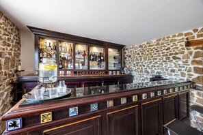 Eine Bar mit Steinwand, Holzbartheke und verschiedenen Flaschen und Gläsern.