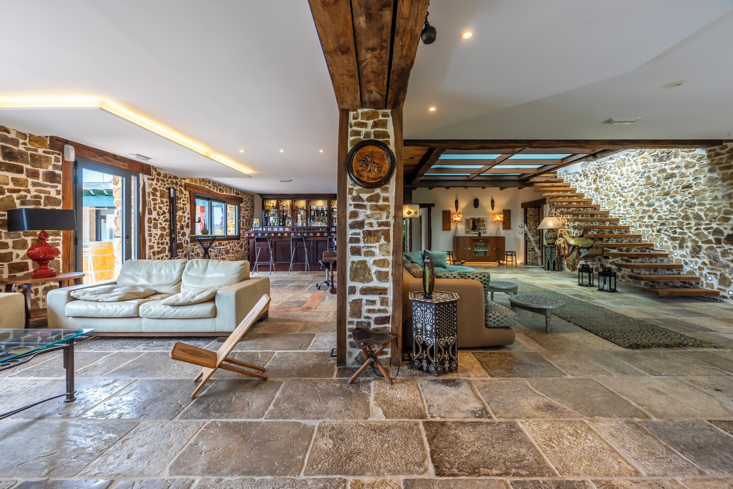 A spacious living area with stone walls, a bar, and a staircase leading to an upper level.