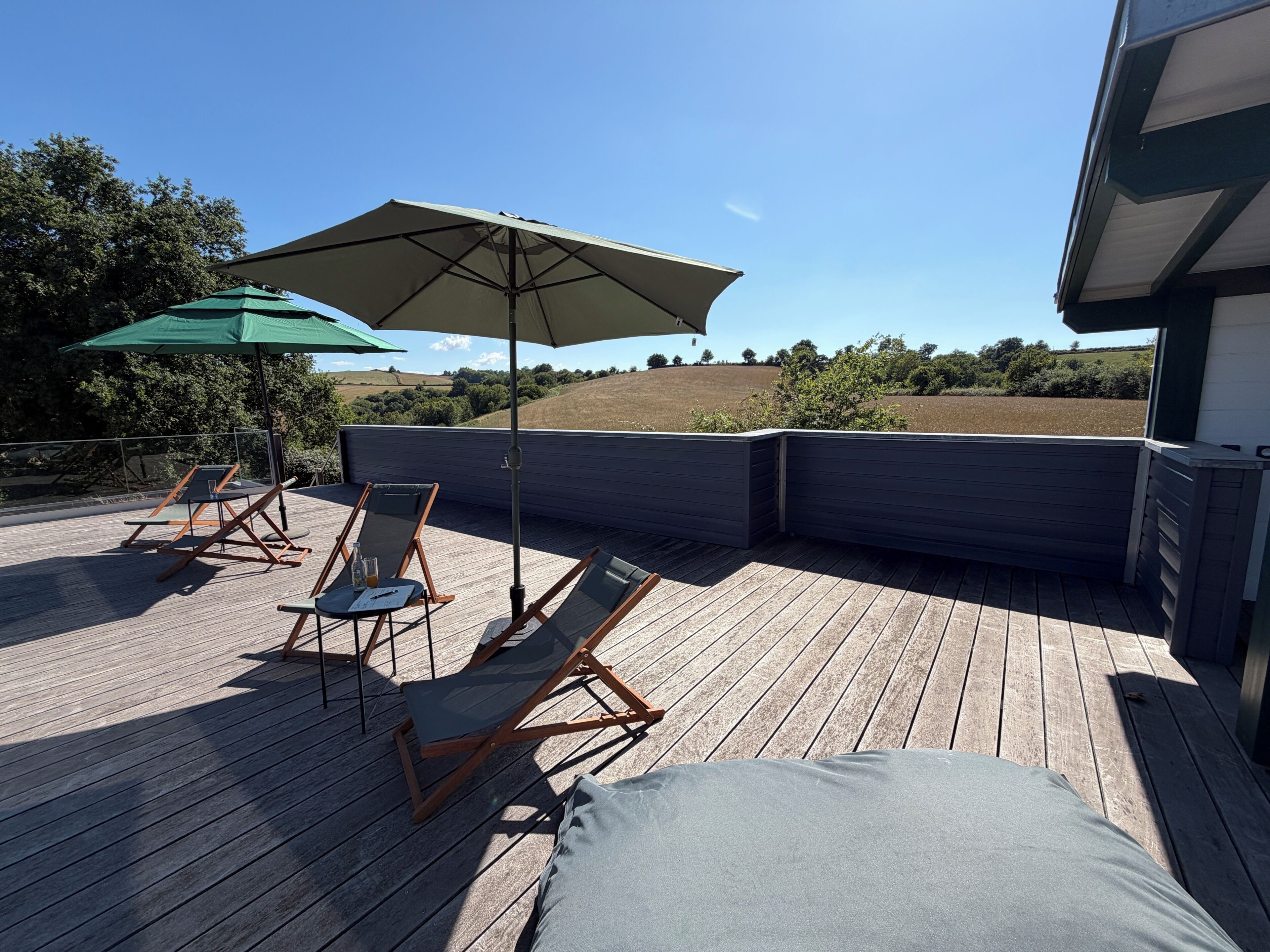 Terraza de madera con sillones de descanso y una sombrilla, con vistas a un paisaje montañoso.