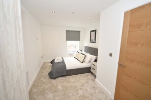A bedroom with a bed, bedside tables, a window with a view, and a door. - Stylish 1 Bedroom Apartment in Central Leeds (Leeds)