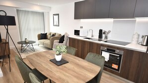 Een moderne keuken met een eethoek, met een houten tafel, stoelen, een kleine potplant en een inbouwoven.