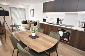 A modern kitchen with a dining area, featuring a wooden table, chairs, a small potted plant, and a built-in oven. - Stylish 1 Bedroom Apartment in Central Leeds (Leeds)