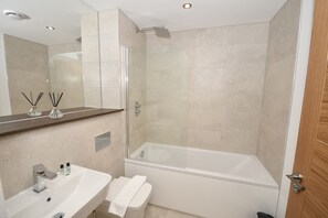 A modern bathroom with a glass-enclosed shower, a white sink with a mirror above it, and a wooden door. - Stylish 1 Bedroom Apartment in Central Leeds (Leeds)
