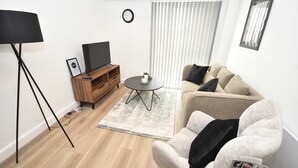 Een moderne woonkamer met een flatscreen televisie, een bank, een salontafel en een vloerlamp.