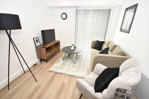 A modern living room with a flat-screen TV, a sofa, a coffee table, and a floor lamp. - Stylish 1 Bedroom Apartment in Central Leeds (Leeds)