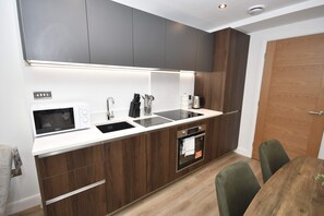 Uma cozinha compacta com micro-ondas, pia e forno, armários de madeira e um espaço de refeições com mesa e cadeiras.