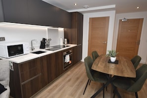 A modern kitchen with a built-in microwave, sink, and stove, and a dining area with a wooden table and green chairs. - Stylish 1 Bedroom Apartment in Central Leeds (Leeds)
