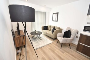 Uma sala de estar moderna com sofá, poltrona, mesa de centro, luminária de chão e uma TV sobre um móvel.