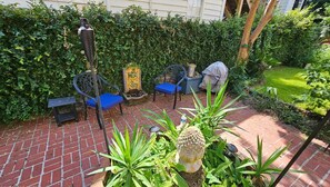 A patio with brick flooring, two blue chairs, a decorative stone, and lush greenery. - Hidden Treasure at Forsyth Park (Savannah)