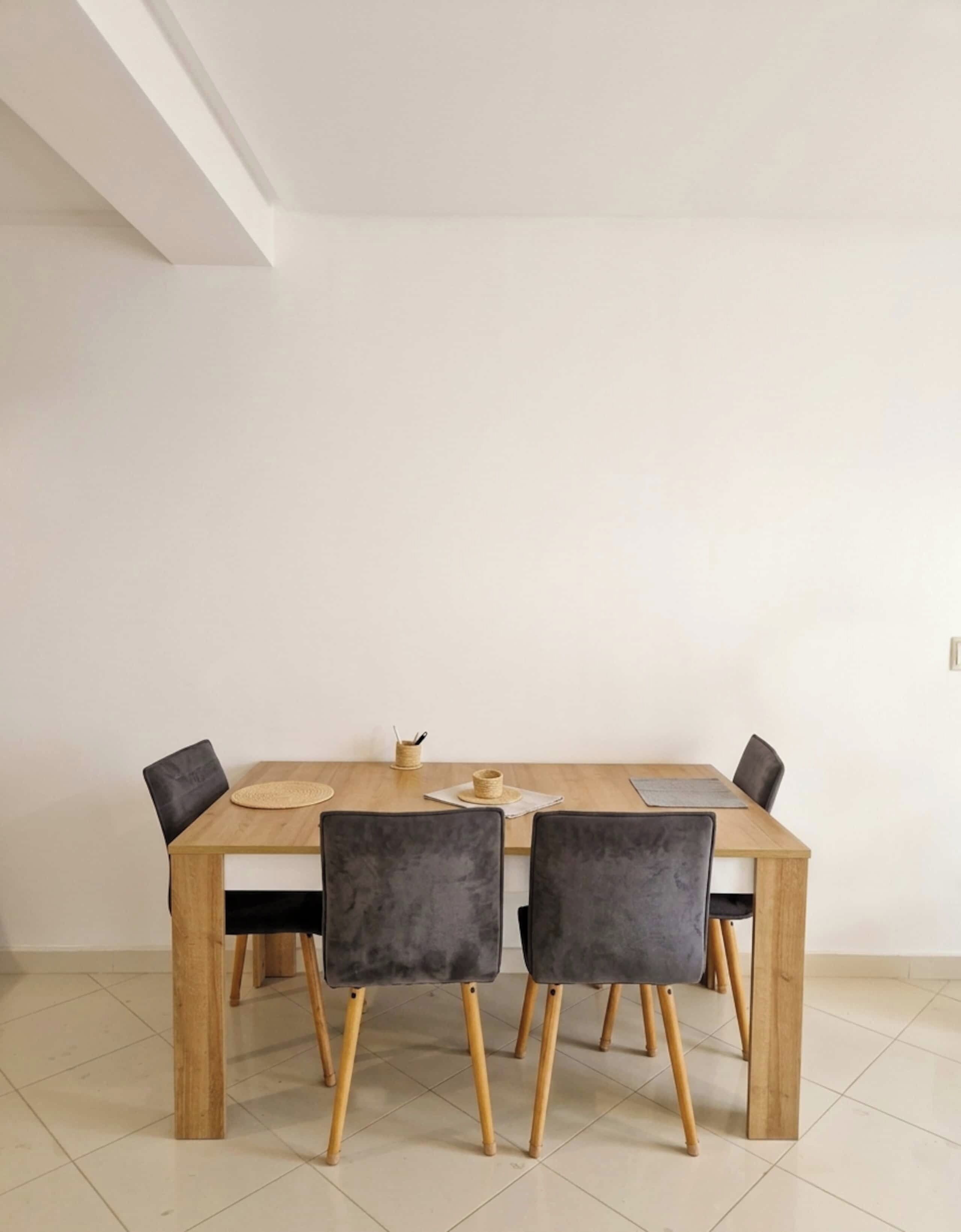 A dining area with a wooden table and four chairs, a woven placemat, and a small woven basket on the table.