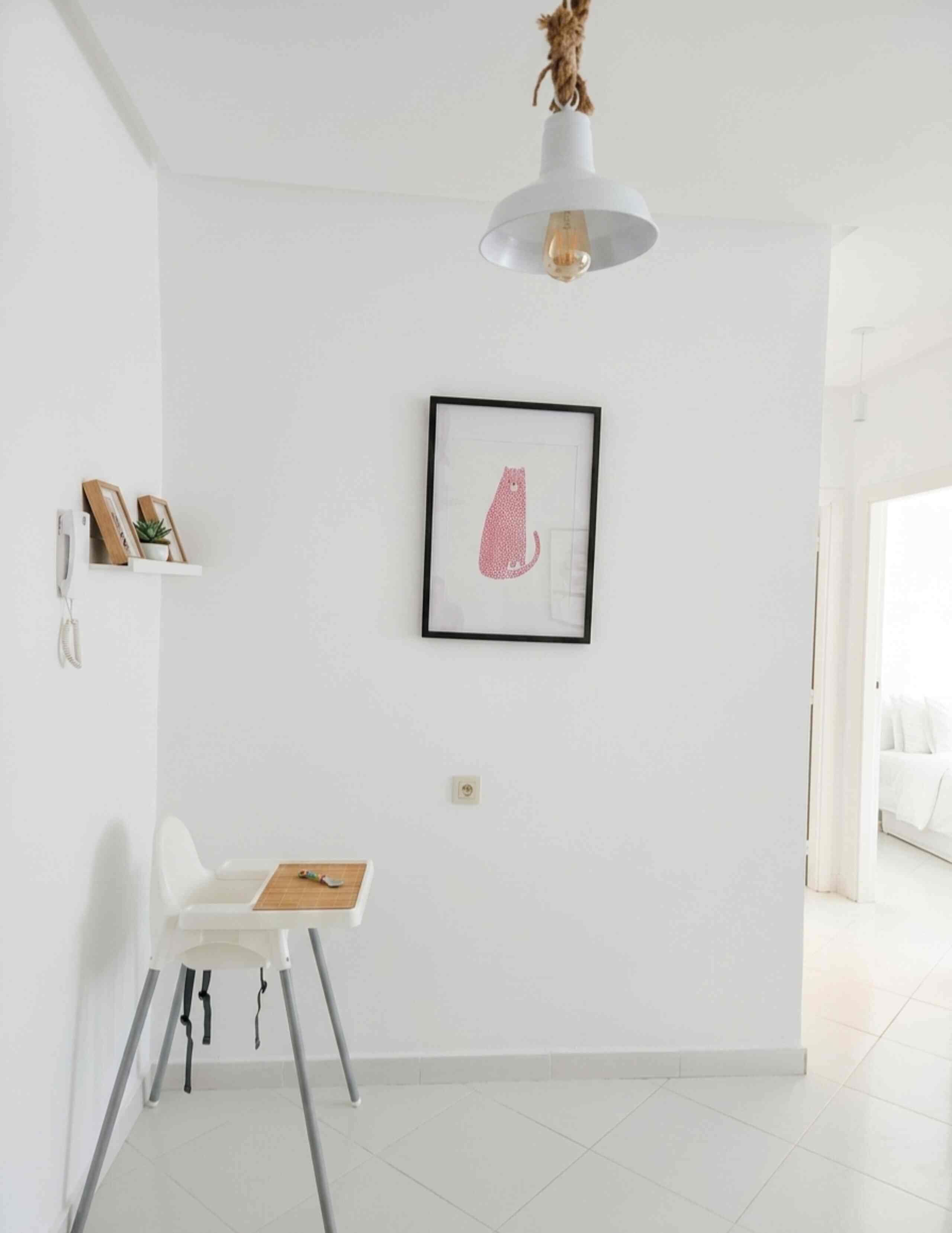 A minimalist room with a white wall, a framed picture, a white chair, and a small table.