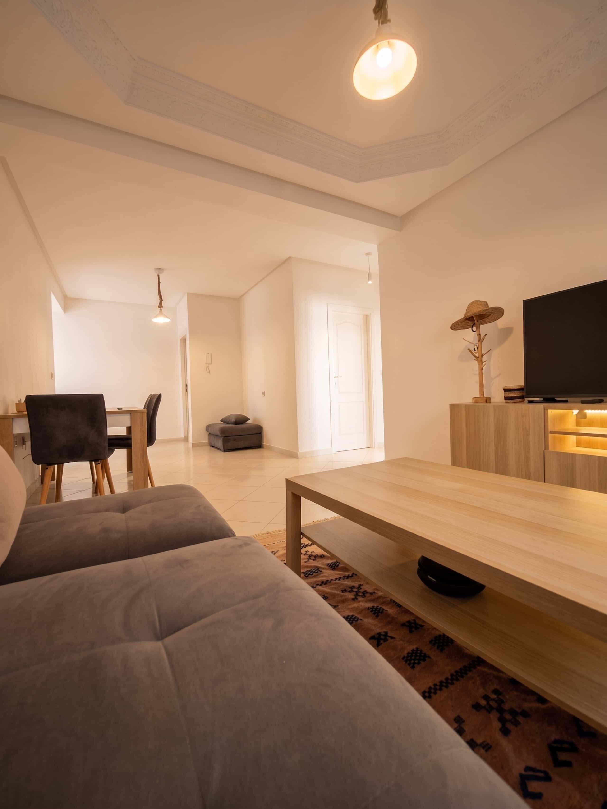 A modern living room with a sofa, a coffee table, a TV, and a dining area with chairs and a table.